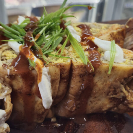Close-up of Breakfast Enchiladas topped with green onions, sour cream, and Tex Mex sauce, served on a wooden board. The enchiladas are filled with breakfast sausage, scrambled eggs, and Monterey Jack cheese.
